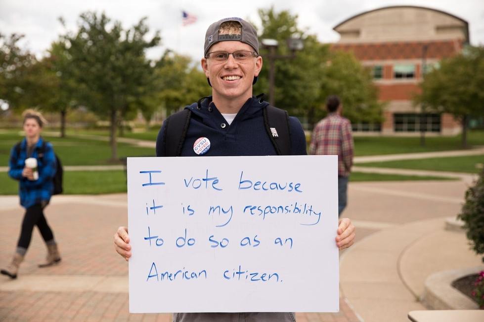 Student holding a sign reading "I vote because it is my responsibility to do so as an American citizen"